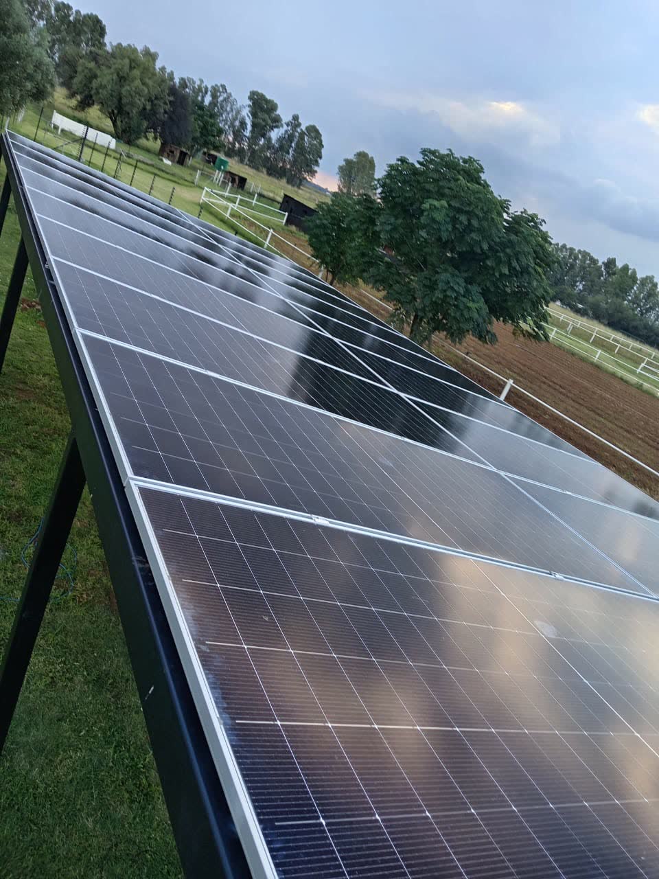 A ground-mounted solar array on a farm under a clouded sky