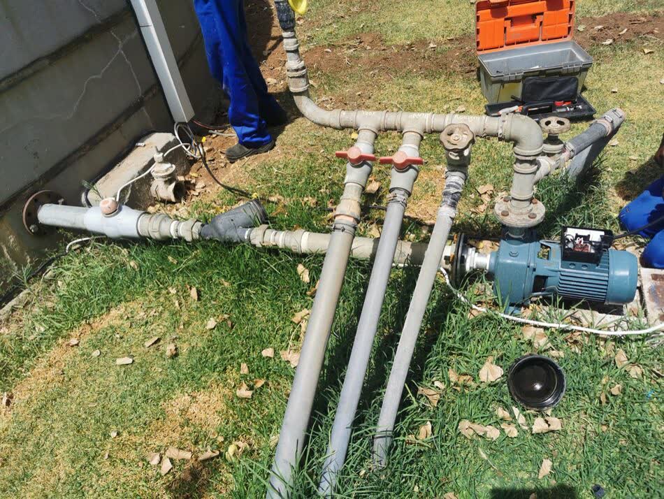 Pipe manifold with multiple valves connected to a pump, laid out on grass on site