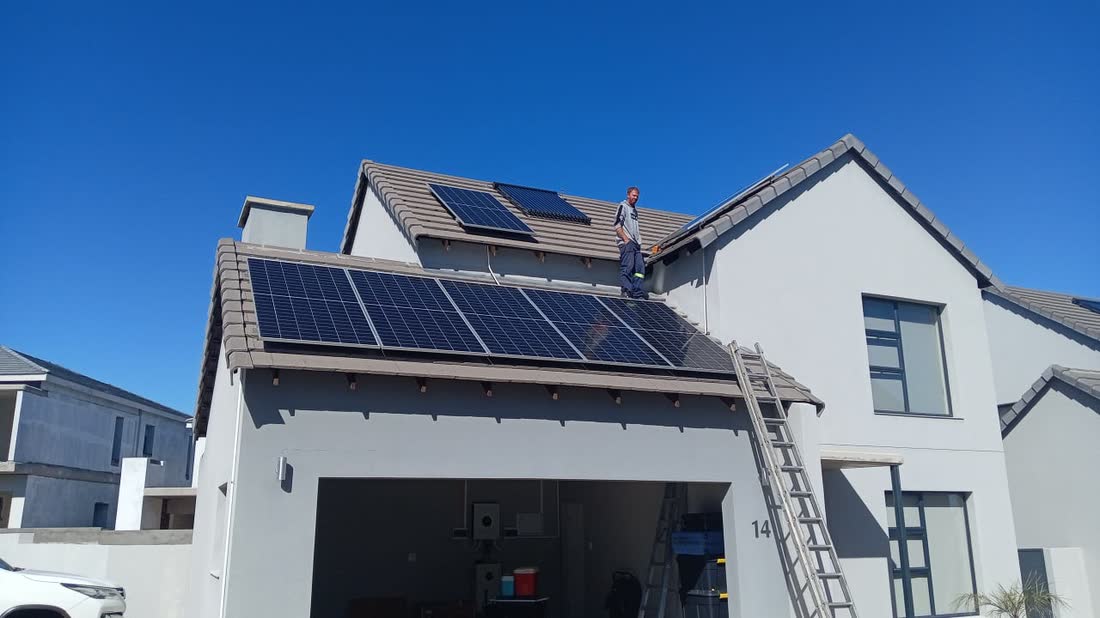 Solar panels being installed on a tiled roof with a ladder against the wall