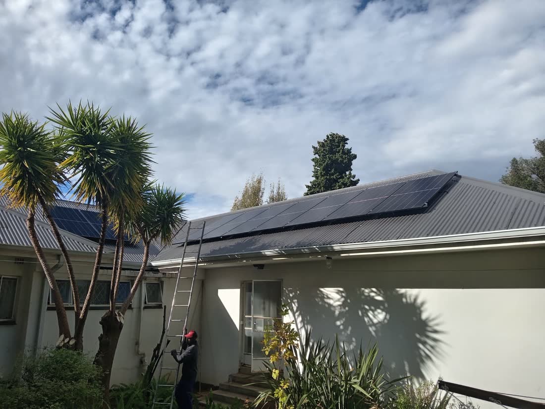 Solar panels on a house roof seen past palm trees under a cloudy sky